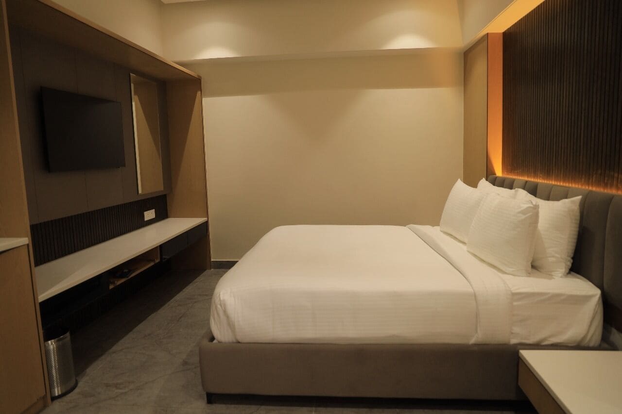 A hotel room with a bed, a TV mounted on the wall, and a small table.