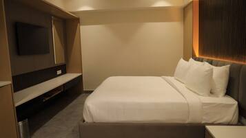 A hotel room with a bed, a TV mounted on the wall, and a small table.