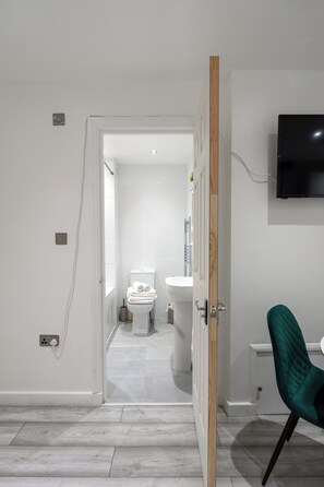 Een moderne badkamer met toilet, wastafel en douche. Een groene stoel is in de voorgrond te zien.