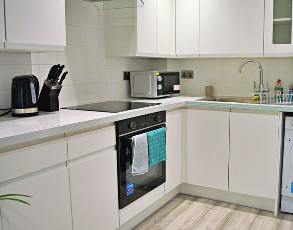 A modern kitchen with white cabinets, a microwave, a kettle, a sink, and a dishwasher.