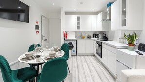 A modern kitchen with white cabinets, a built-in oven, and a sink. There is a dining table with chairs and a TV mounted on the wall. - Beautiful Flat in London- Close to Central London- Canary Wharf- London ExCel (London)