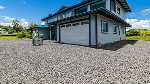 A modern two-story house with a garage, surrounded by gravel and greenery. - Hilo Town Center Studio (Hilo)