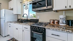 A modern kitchen with white cabinets, a gas stove, a microwave, and a coffee maker. - Hilo Town Center Studio (Hilo)