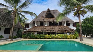 A resort with a pool, thatched-roof buildings, and palm trees. - Milele beach resort  (Dongwe)