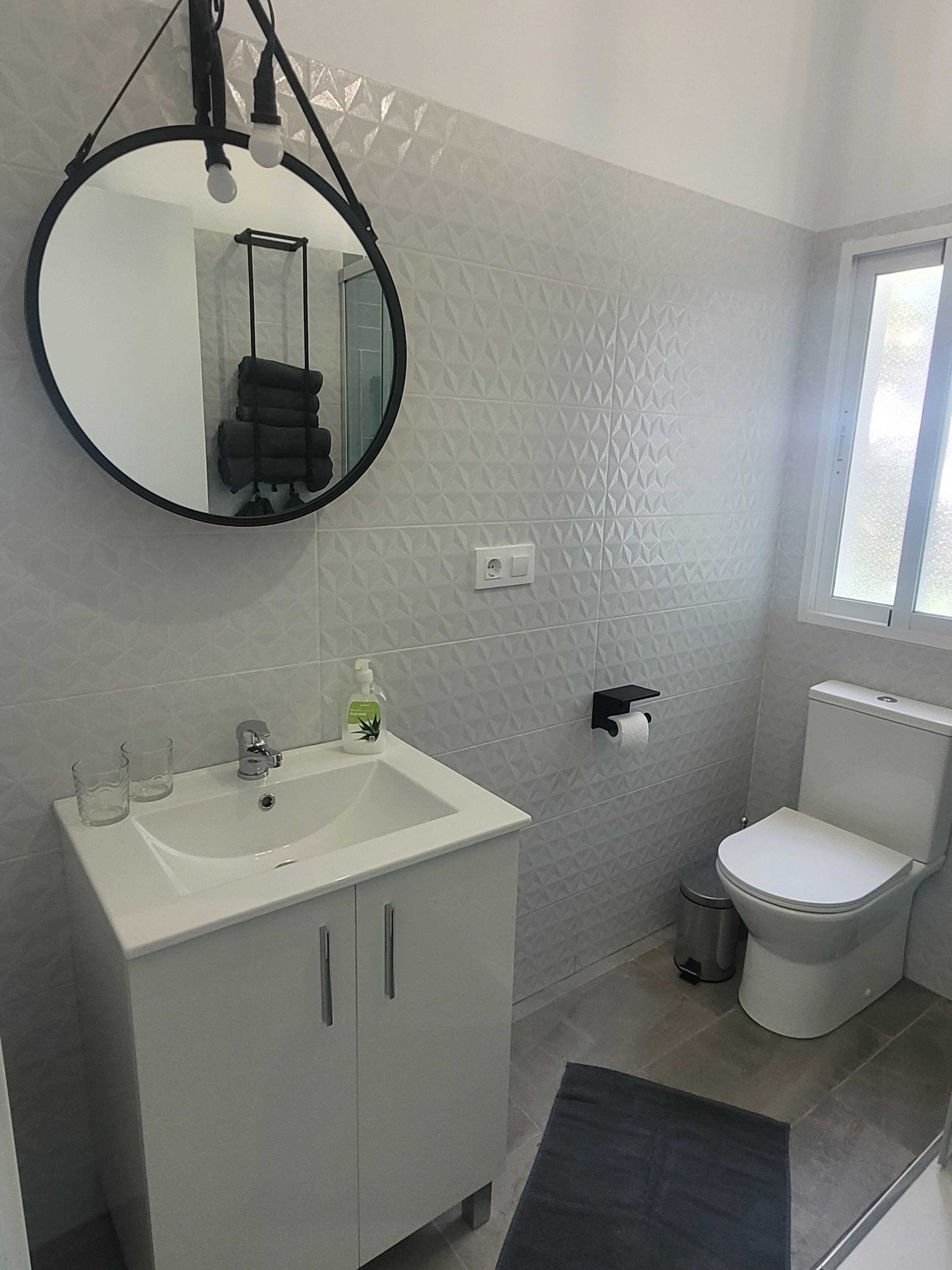Un baño con un lavamanos blanco, un espejo, un inodoro y una ventana.