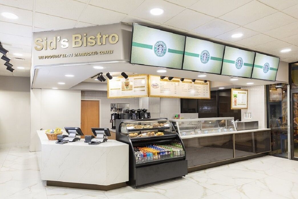Un café Starbucks avec un comptoir, des panneaux affichant le menu et une vitrine où sont présentées les pâtisseries.