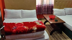 A hotel room with two beds, each with white bedding and a red floral blanket on one bed. There is a small wooden table with a red decorative item and a green object on it. - SS Hotel Kings & Lodge Charikot Dolakha (Bhimeshwar)