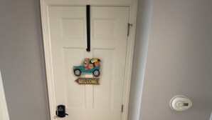 Eine weiße Tür mit einem 'WELCOME'-Schild und einer kleinen Spielzeugauto-Dekoration.
