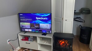 Ein Wohnzimmer mit Flachbildfernseher auf einem Standfuß, einer weißen Unterhaltungseinheit darunter, einem schwarzen Kaminofen und einer weißen Tür im Hintergrund.