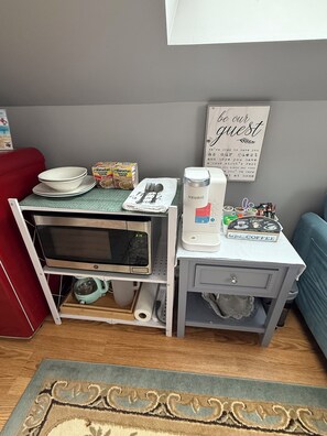 A compact kitchenette with a microwave, coffee maker, and storage for bowls and cereal boxes.