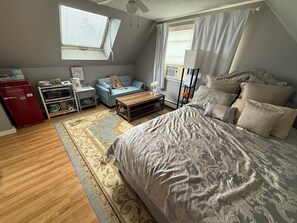 Une chambre à coucher avec un lit, un bureau, un canapé, un réfrigérateur rouge et une fenêtre avec des stores.