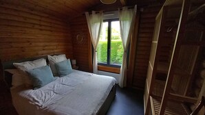 A wooden cabin bedroom with a bed, pillows, a window with curtains, and a wooden ladder.