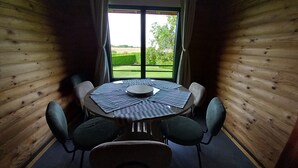 A wooden-paneled room with a round table and four chairs, a window with curtains, and a view of greenery outside.