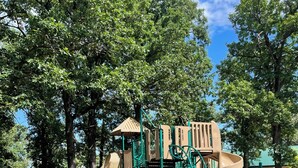 A playground with a slide and climbing structures, surrounded by trees and a picnic table in a park. - Cozy 2-bd home in Newfolden. WiFi, AC, Full kitchen & living room w fireplace!  (Newfolden)