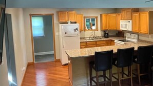 A kitchen with wooden cabinets, a refrigerator, a microwave, and a stove. There are four bar stools and a window with a view. - Cozy 2-bd home in Newfolden. WiFi, AC, Full kitchen & living room w fireplace!  (Newfolden)