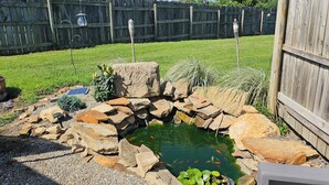 A backyard with a pond surrounded by rocks, a wooden fence, and a solar-powered water pump. - #5 getaway cabin 
 (New Lexington)