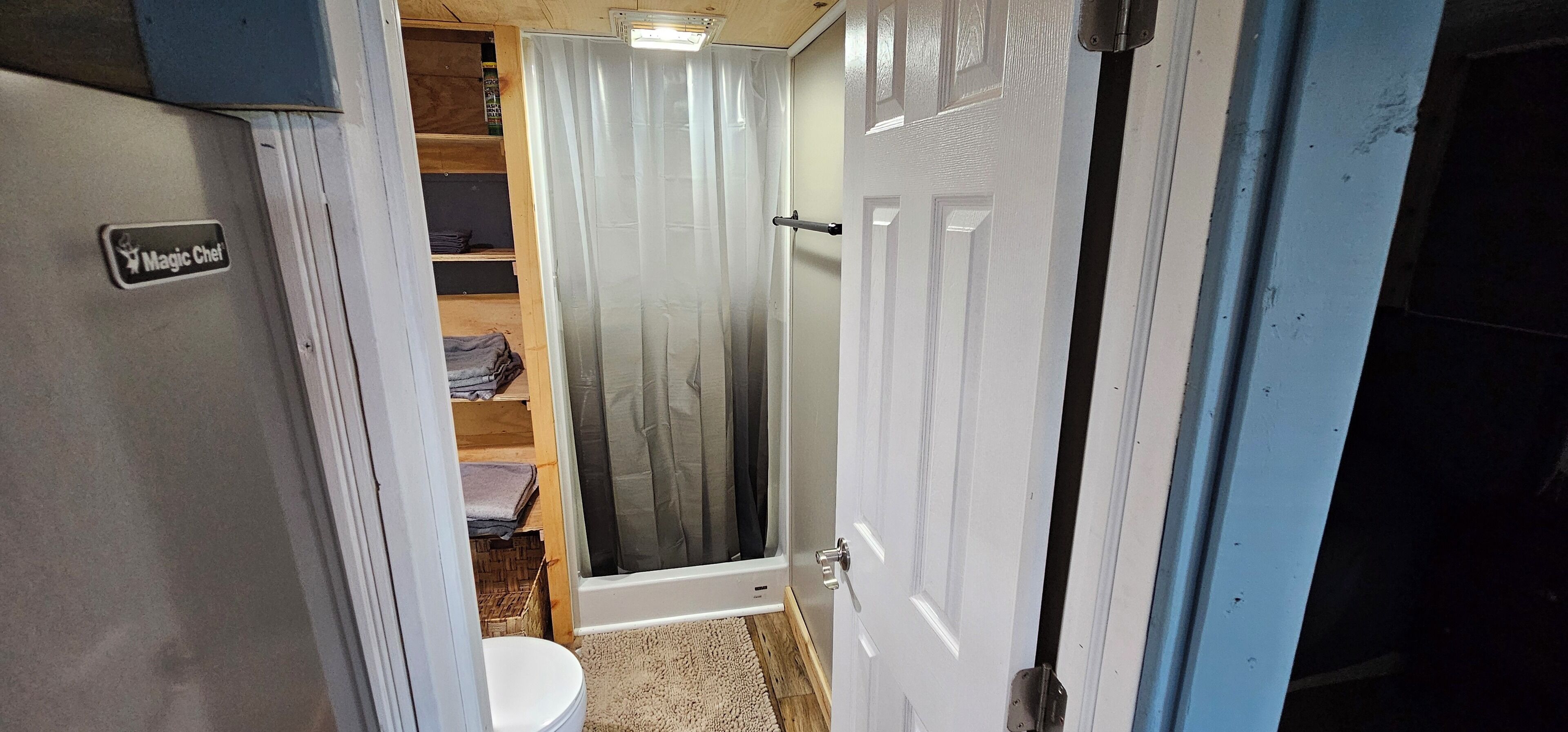 A bathroom with a toilet, a shower, and a storage shelf.