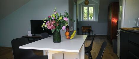Ein Essbereich mit einem weißen Tisch, schwarzen Stühlen, einer Blumenvase und einer Obstschale.