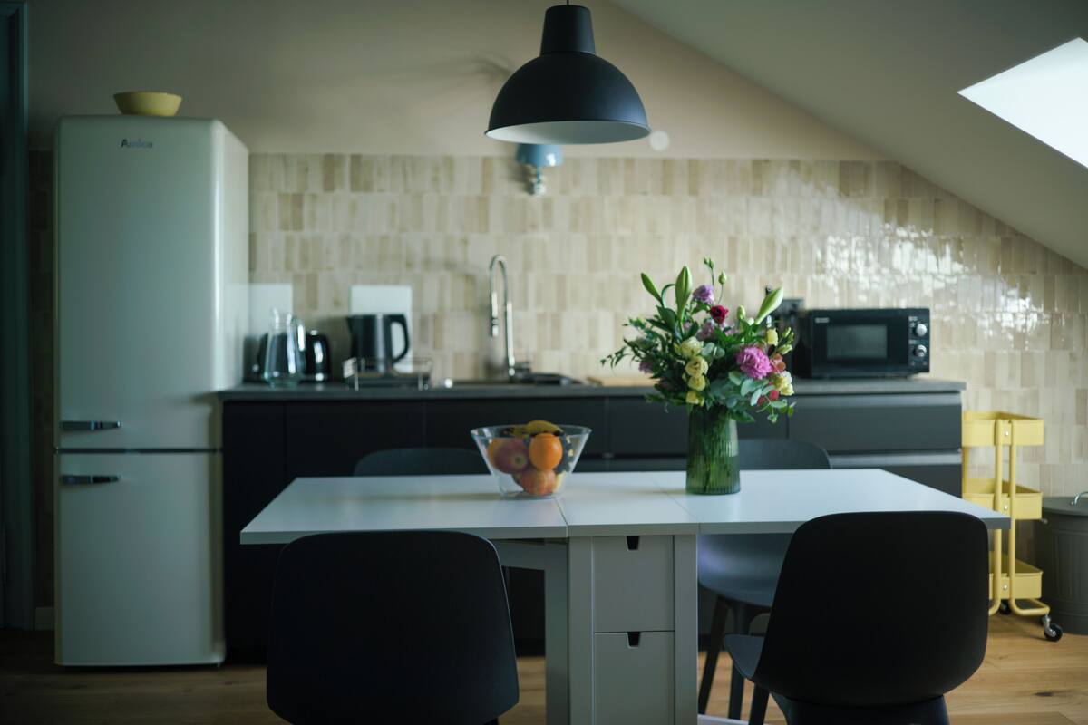 A modern kitchen with a dining area, featuring a white refrigerator, a microwave, a sink, and a dining table with chairs.