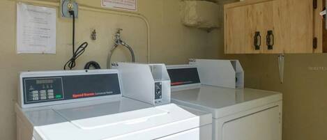 Un espace buanderie compact comprenant deux lave-linge professionnels de marque Speed Queen, un meuble contenant des produits de nettoyage et un panneau d’avertissement concernant l’utilisation de la lessive.