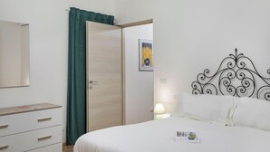 A bedroom with a bed, a dresser, a door, and a wall with a decorative headboard and a framed picture. - Casa Alma by Wonderful Italy (Genoa)