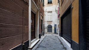 A narrow alleyway with closed shuttered buildings on both sides, a cobblestone path, and a small door at the end. - Casa Alma by Wonderful Italy (Genoa)