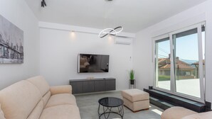Un salon moderne avec un canapé, une table basse, un téléviseur et une grande fenêtre donnant sur des immeubles.