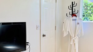 A modern living room with a flat-screen TV on a white cabinet, a striped rug, a beige sofa, and a white robe hanging on a rack. - Cozy studio in adorable Nevada City with AC, WiFi (Nevada City)