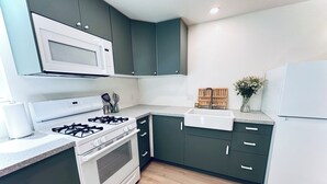 A modern kitchen with dark green cabinets, a white gas stove, a microwave, and a built-in sink. - Cozy studio in adorable Nevada City with AC, WiFi (Nevada City)