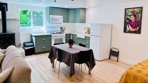A compact kitchen with a microwave, stove, and refrigerator. A dining table with chairs is set up in the center. - Cozy studio in adorable Nevada City with AC, WiFi (Nevada City)