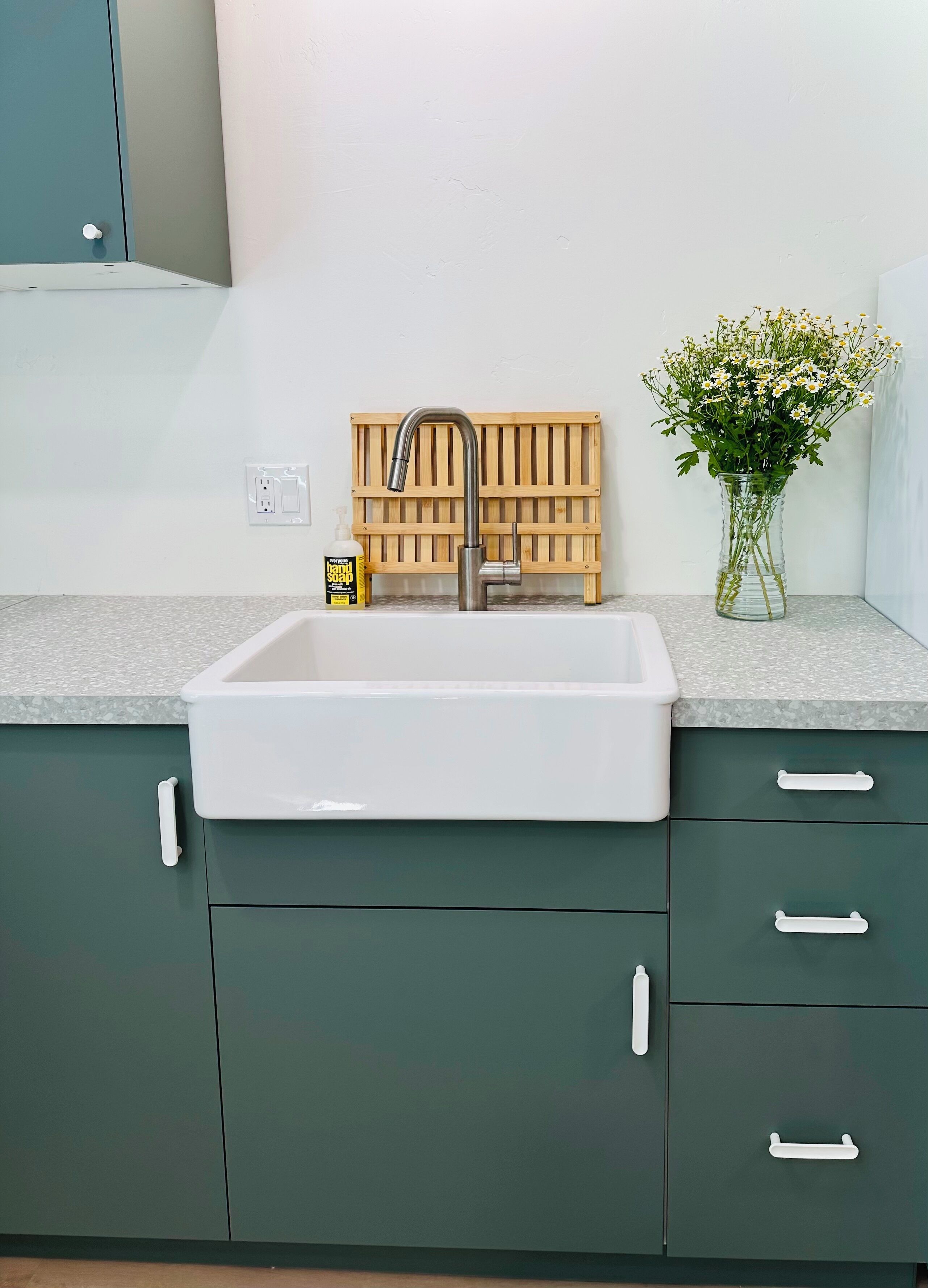 Een keuken met een witte spoelbak, donkergroene kastjes en een houten wandpaneel.