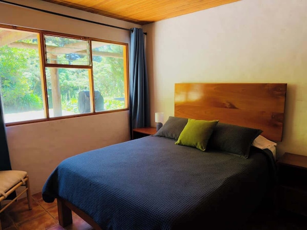 Ein Schlafzimmer mit einem großen Bett, einem Holzkopfteil, einem Fenster mit Vorhängen und einem Sessel.