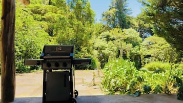 Una barbacoa portàtil sota una estructura de fusta amb vista a un jardí exuberant.