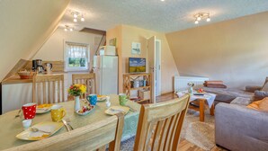 A cozy, well-lit dining area with a table set for two, a kitchen in the background, and a living area with a sofa and a TV. - Cozy home in Dabel with WiFi (Dabel)