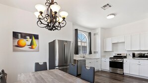 A modern kitchen with white cabinets, stainless steel appliances, and a wooden dining table.