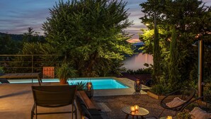 A poolside area with seating, a sign with symbols, and a view of a lake at dusk. - Luxurious home in Bakarac with private swimming pool, can be inside or outside (Bakarac)