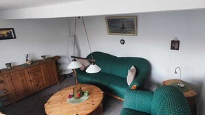 Un salon chaleureux avec un canapé vert, une table d’appoint en bois et une table basse ronde en bois.
