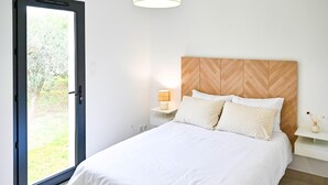 Een slaapkamer met een bed, nachtkastje, lamp, houten hoofdbord en een deur naar een tuin.