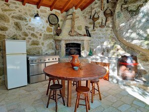 Une cuisine rustique en pierre, avec un mur en pierre, une table en bois et des tabourets, un réfrigérateur blanc, une cuisinière et un grand tonneau en bois.