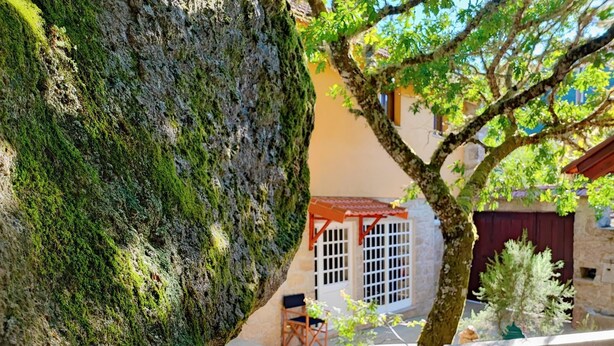 Un banco de piedra, un árbol y un edificio con tejado rojo y ventanas blancas.