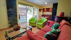 Una sala de estar con un sofá, dos sillones, una mesa de centro y vistas a una cocina y un espacio exterior.