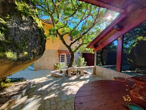 Une cour avec un sol en pierre, une table en bois et un arbre qui offre de l’ombre.