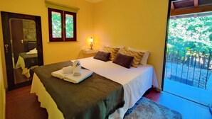 Un dormitorio con cama, lámpara de noche, ventana y vista a zonas verdes.