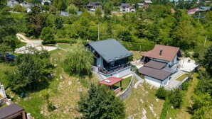 An aerial view of a residential area with two modern houses, surrounded by lush greenery and a winding road.