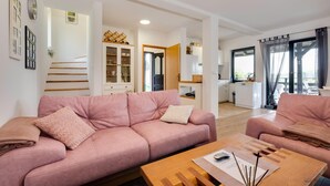 A living room with a pink sofa, a wooden coffee table, and a kitchen visible in the background.