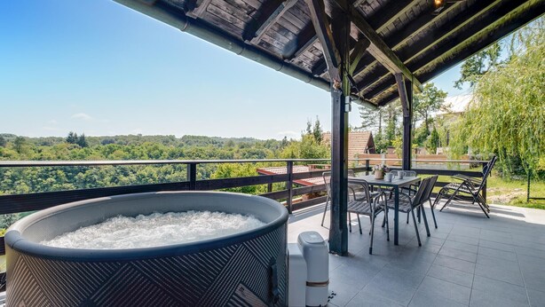 A hot tub on a patio with a table and chairs, overlooking a forested area.