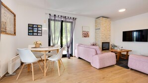 A modern living room with a stone fireplace, a flat-screen TV, and a dining area with a round table and chairs.