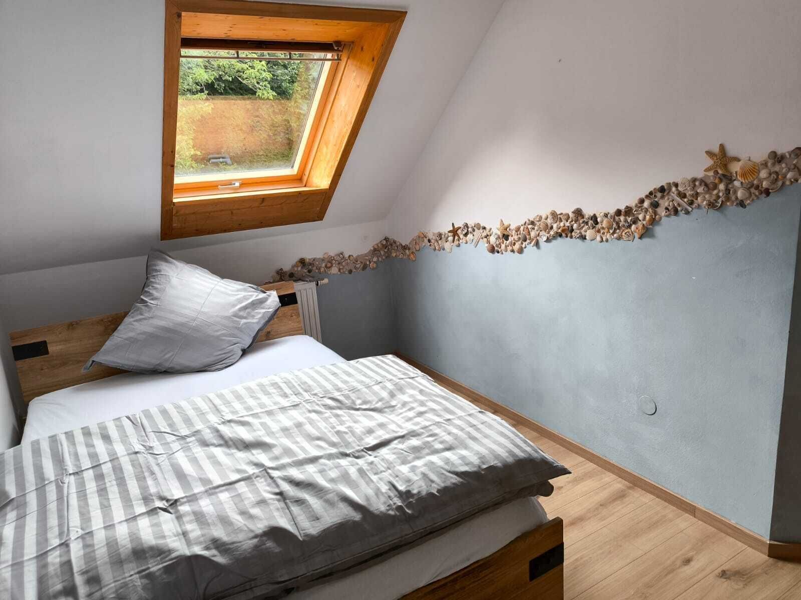 Ein Schlafzimmer mit schräg gedachter Decke, einem Oberlicht, einem Bett mit gestreifter Decke und einer mit Muscheln verzierten Wand.