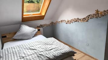 Ein Schlafzimmer mit schräg gedachter Decke, einem Oberlicht, einem Bett mit gestreifter Decke und einer mit Muscheln verzierten Wand.
