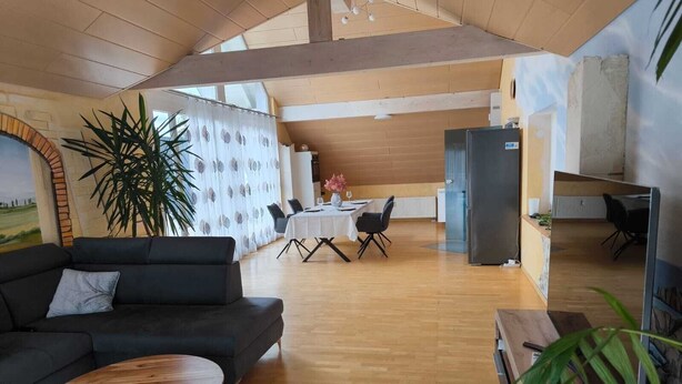 A spacious living area with a black sofa, a wooden coffee table, and a dining table set for four.